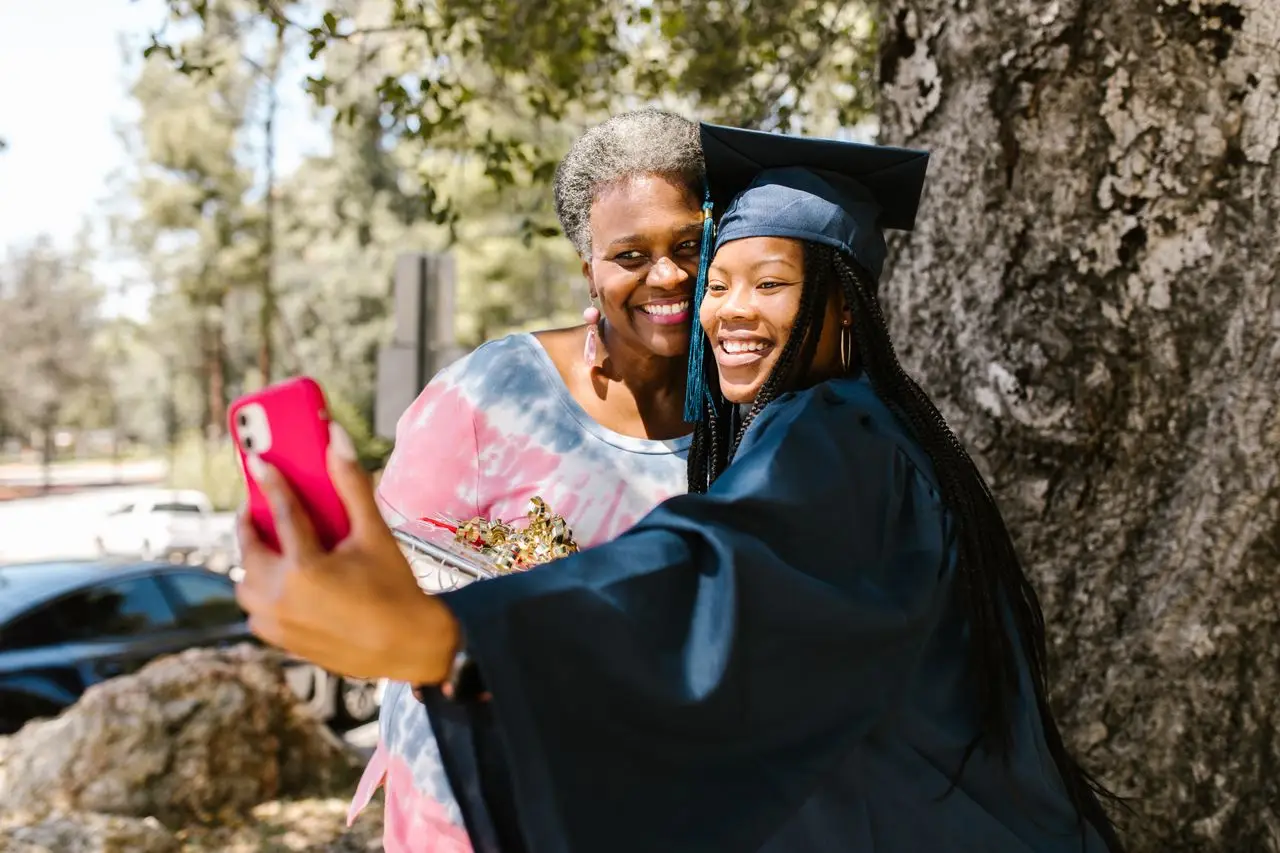 A proud graduate takes a cheerful selfie with family outdoors, capturing a joyful graduation moment