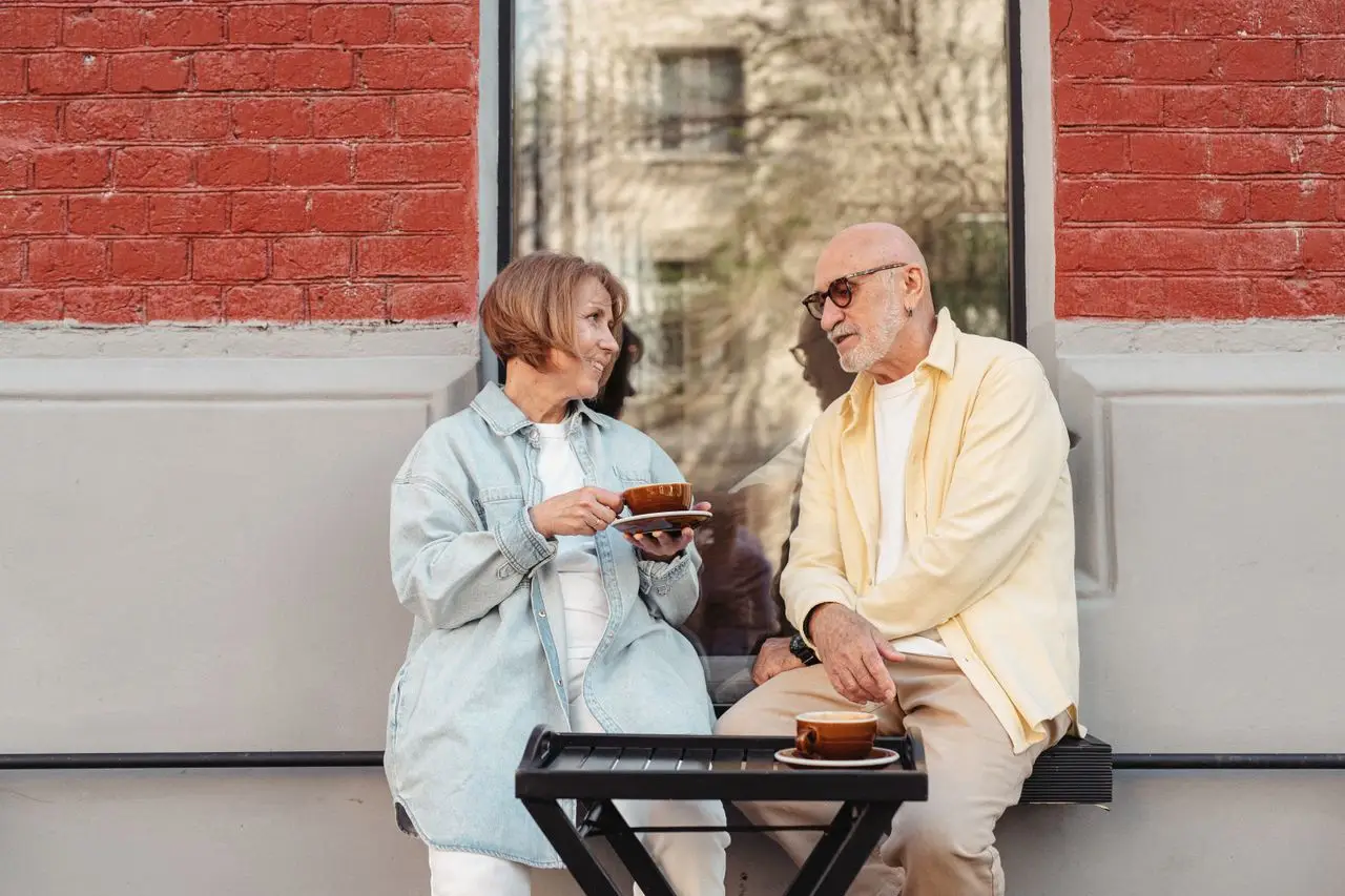 Senior couple sitting outdoors enjoying coffee against a brick wall