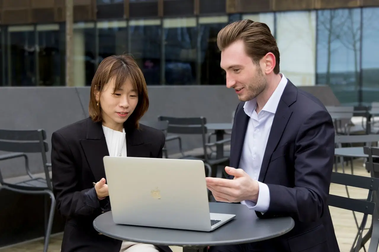 Two professionals collaborating over a laptop during an outdoor business meeting