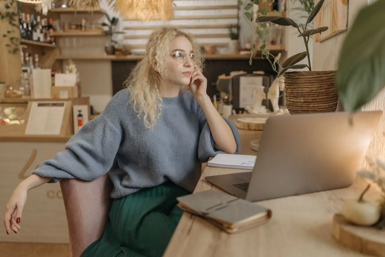 Young woman writing notes on a laptop in a cozy cafe setting