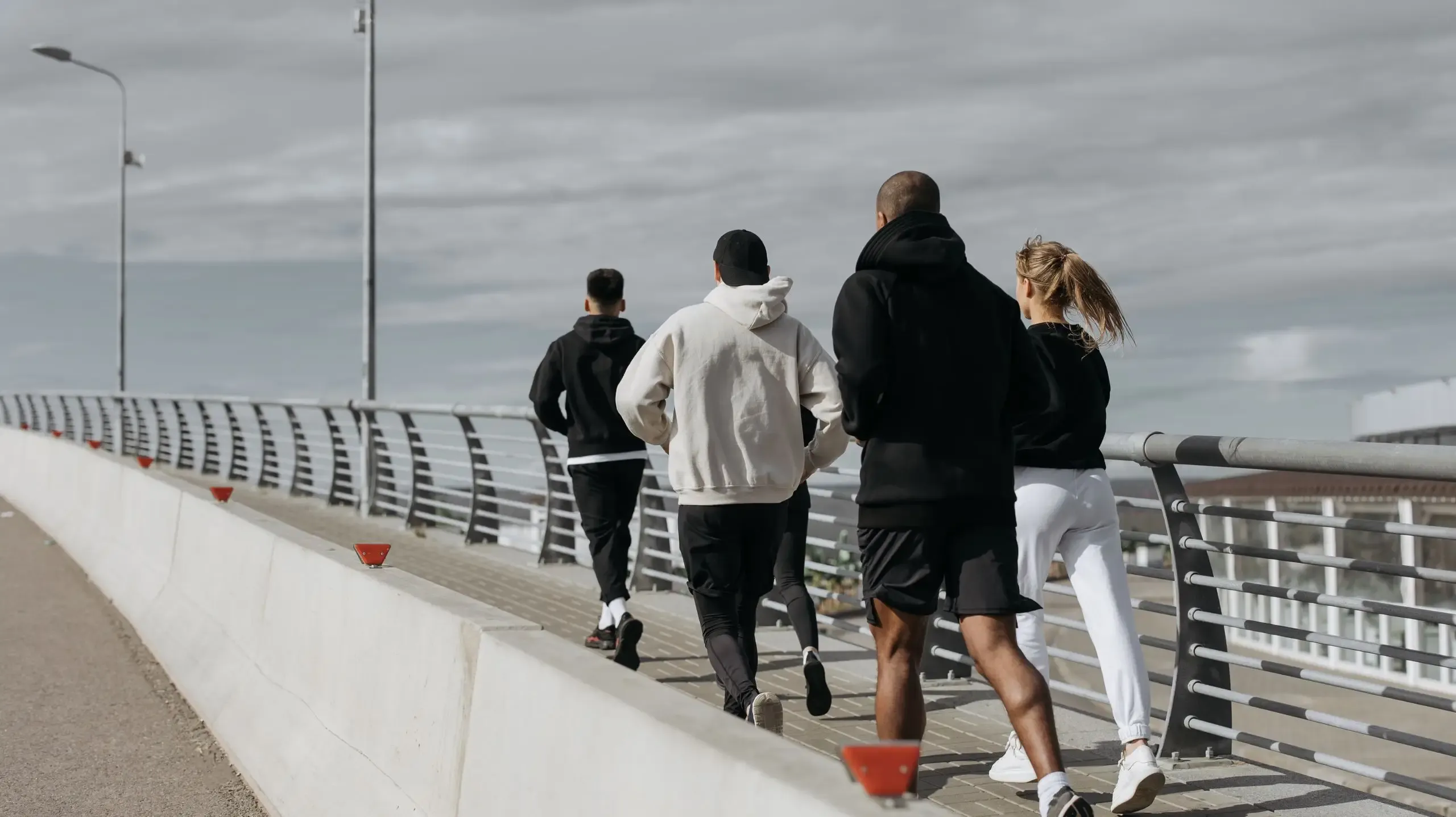 Four individuals walking on a bridge with a city skyline visible in the background.